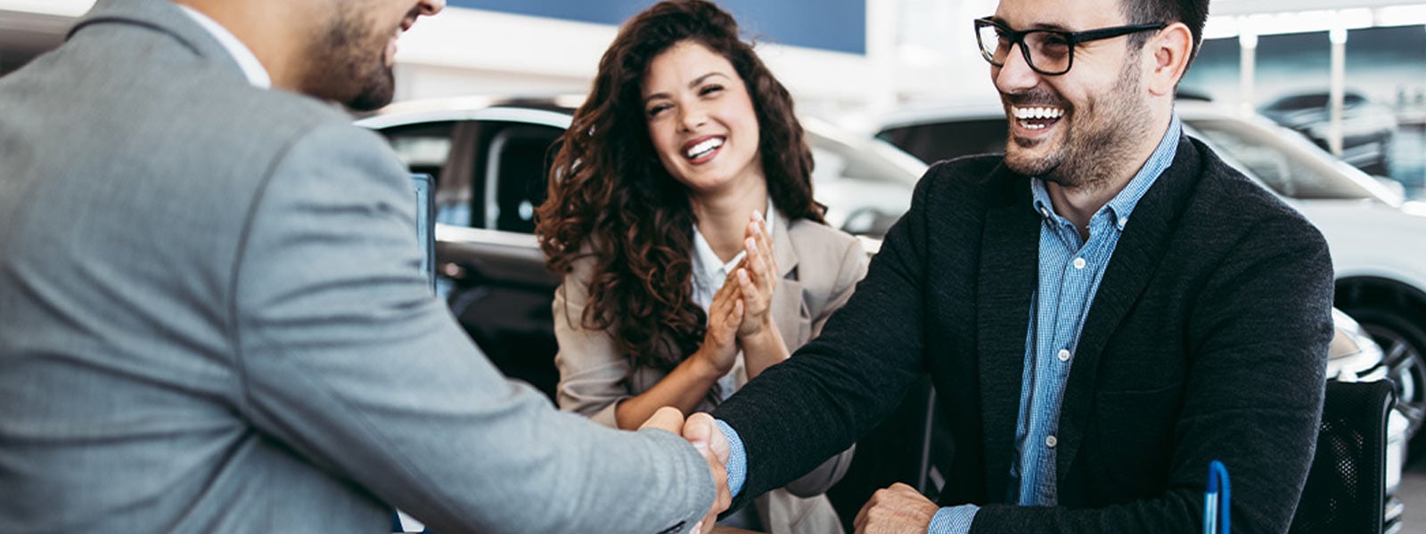 A couple shaking hands with a sales consultant after agreeing how to pay for their new Kia