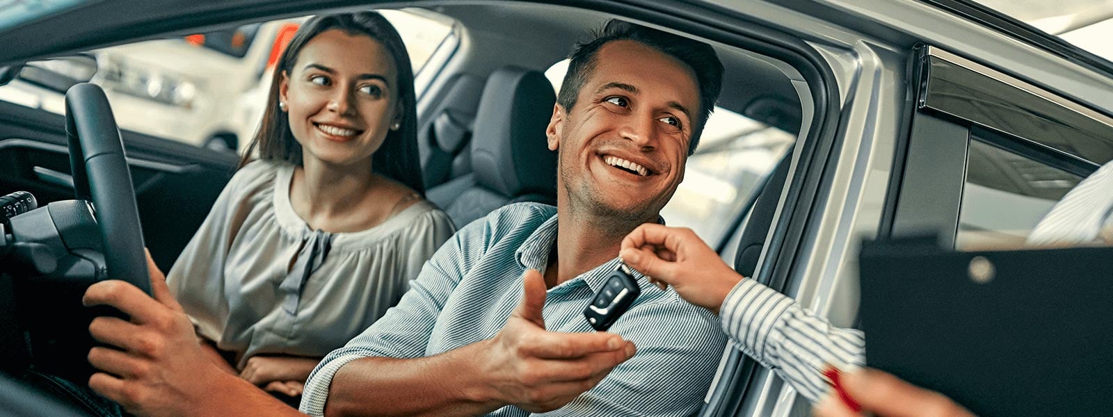 A sales consultant handing the keys through the window to a couple in their new Kia on delivery day