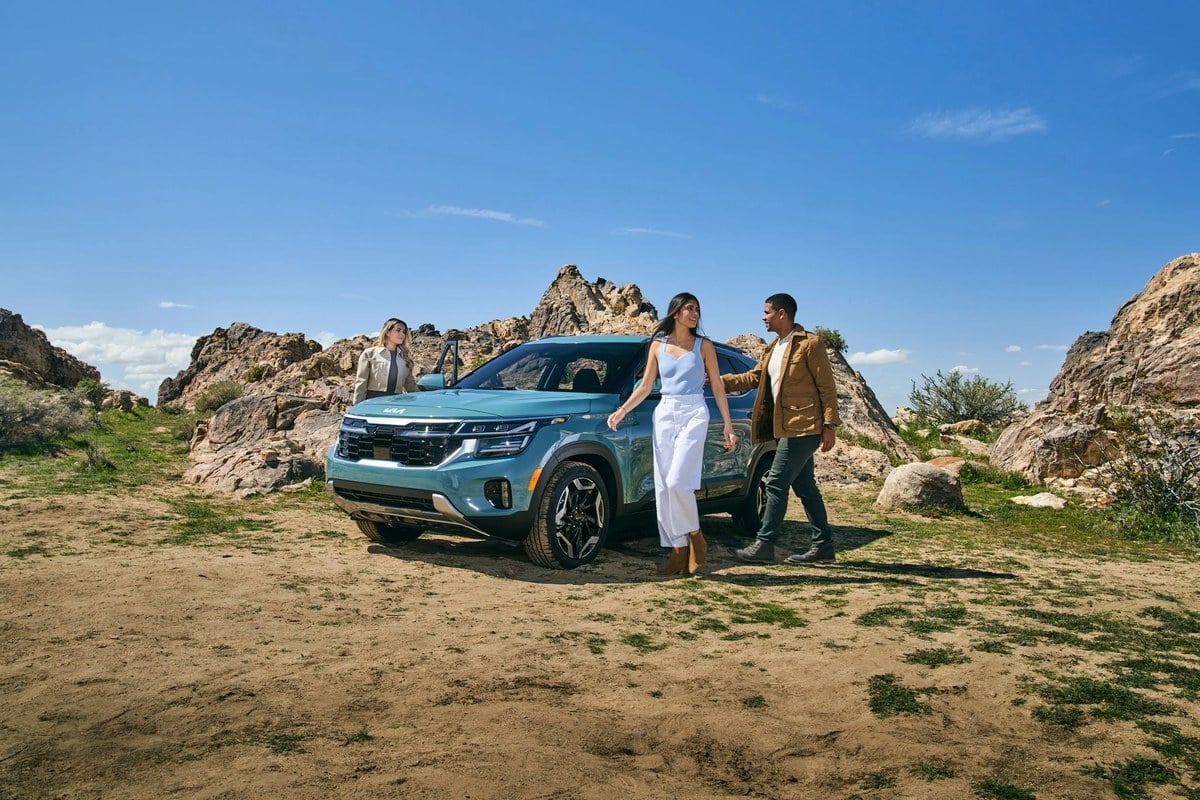 Three friends beside a new Kia Seltos on a back road, the kind of vehicle a lease puts within reach