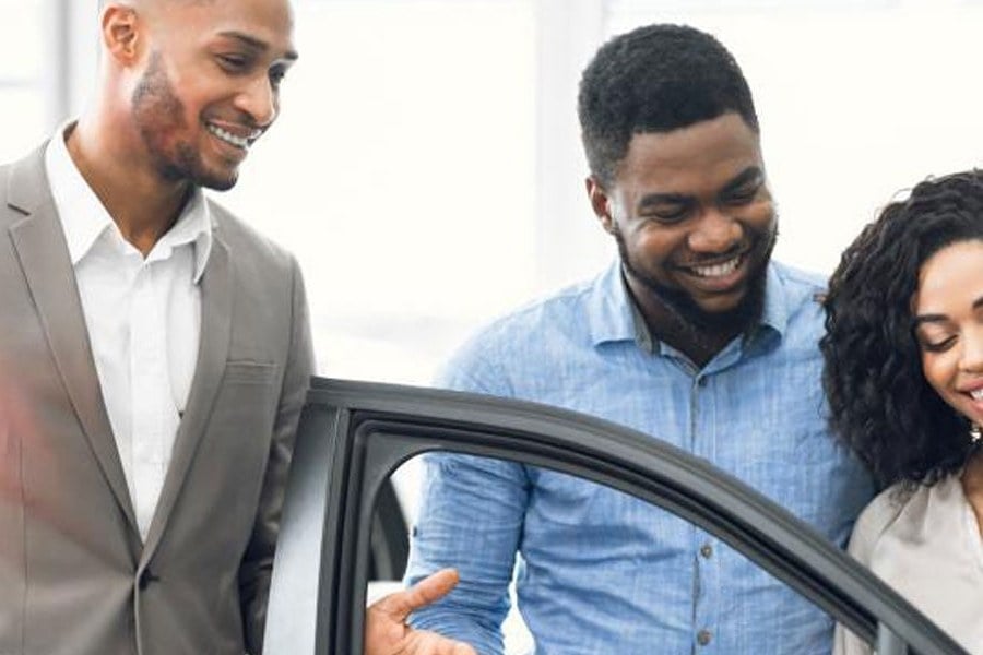 A sales consultant showing a couple around a Kia in the showroom, door open